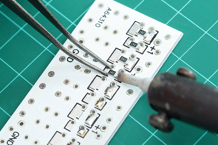 チップ抵抗をピンセットで掴んで、ハンダ付けしているシーン